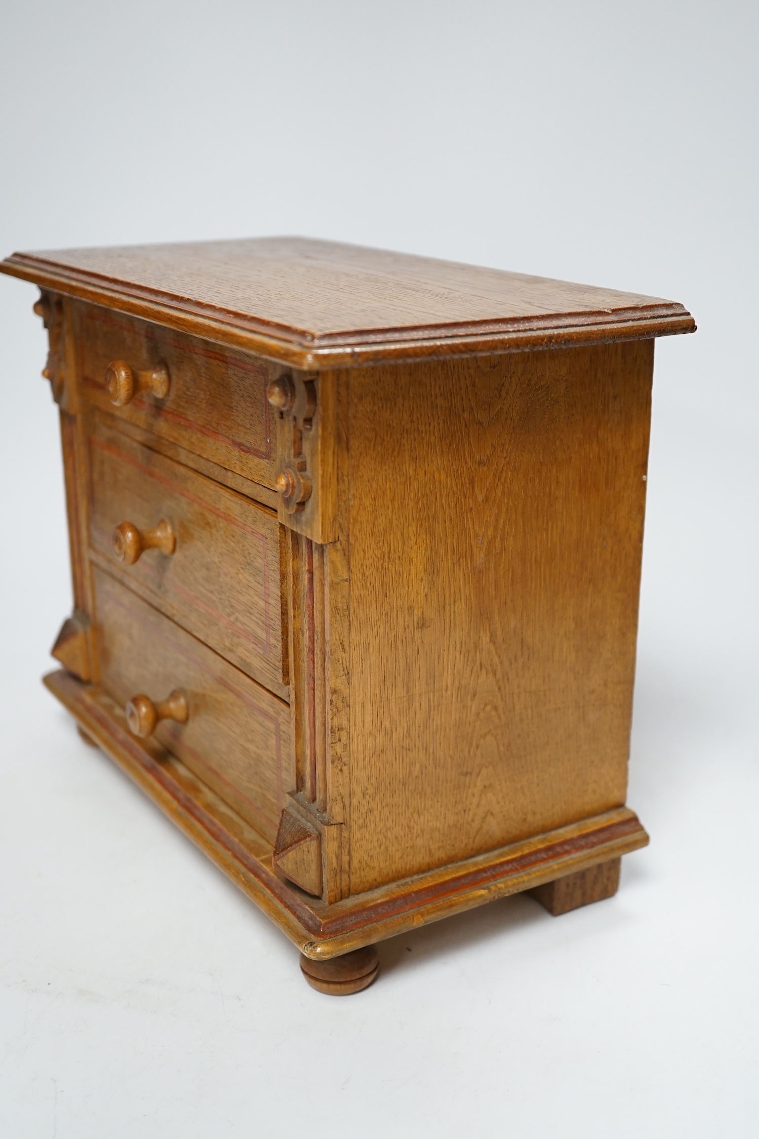 A miniature oak chest of drawers and contents (miniature bisque headed dolls and linen) height 22cm